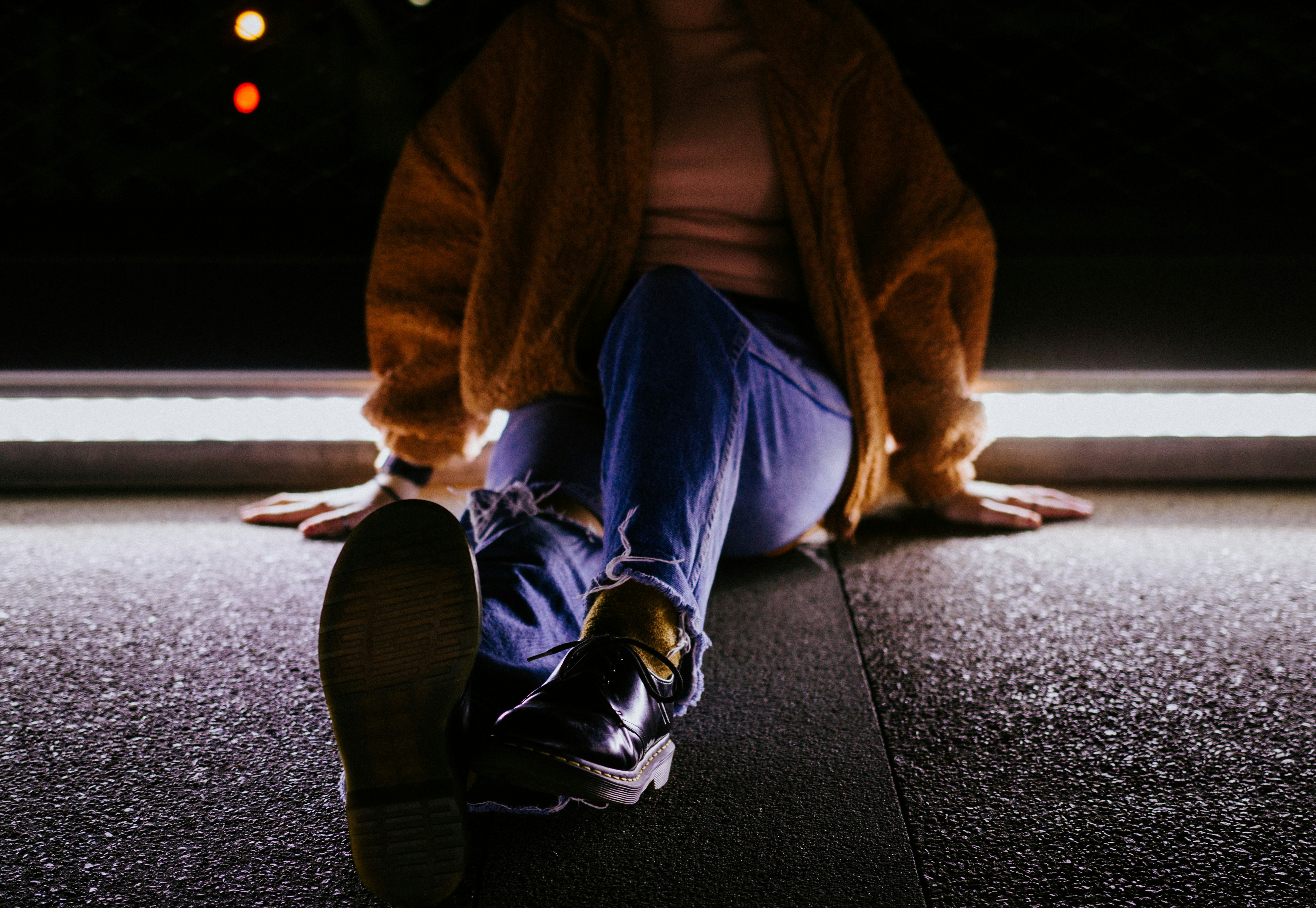 person in blue denim jeans and brown coat sitting on gray concrete pavement